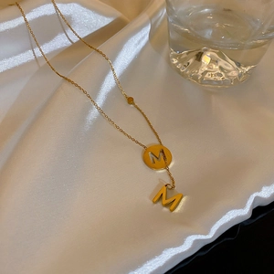 Dettaglio della collana in oro e acciaio al titanio con pendenti a lettera M su seta