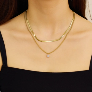 Detail of layered gold herringbone chain and zircon heart pendant necklace on model
