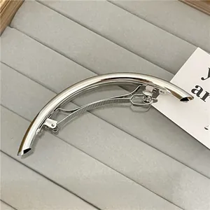 Close-up of polished silver arc hair clip with a spring clasp on grey velvet