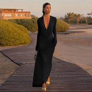 Black long-sleeve maxi dress with deep V-neck and slim fit on a sunset beach walkway