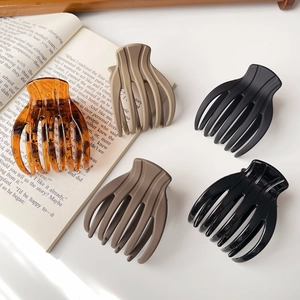 Detailed view of hair claw clips in matte black, khaki, and glossy amber on a book page