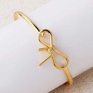 Bracciale a cerchio minimalista placcato in oro con nodo esposto su supporto bianco e sabbia