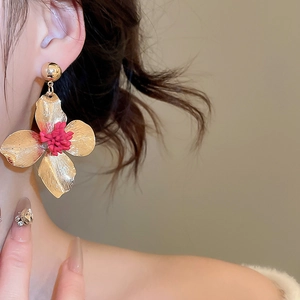 Close-up of a gold flower earring with red stamens worn on a model's ear detail