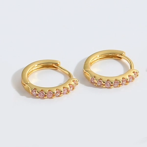 Detailed view of gold huggie earrings with a row of prong-set pink cubic zirconia stones