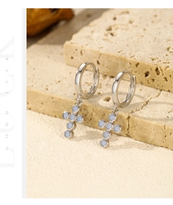 Close-up of s925 silver cross drop earrings with blue opal stones on a beige stone
