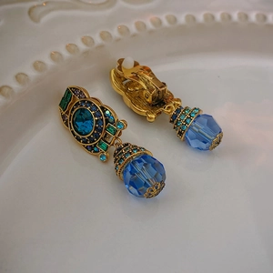 Vintage gold clip-on earrings with blue faceted crystals and rhinestones on ceramic tray