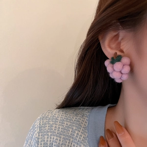 Detail of pink grape-shaped plush earrings worn by a model in soft natural lighting