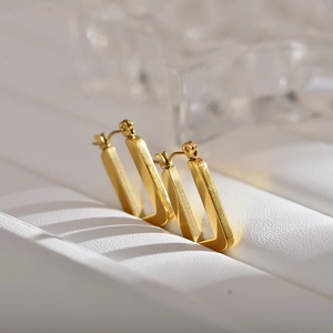 Detailed macro view of gold-plated geometric square earrings with a brushed metal texture