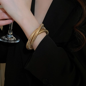 Close-up of a layered gold spiral cuff bracelet with threaded texture on a woman's wrist