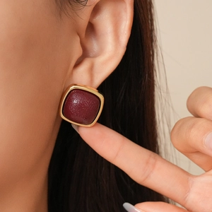 Detail view of retro geometric gold square earrings with red textured leather inlay