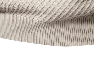Macro view of beige cotton sweater showing rib-knit hem and diamond textured pattern