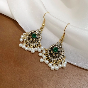 Dettaglio di orecchini vintage dorati con strass verdi e nappe di perle su seta bianca