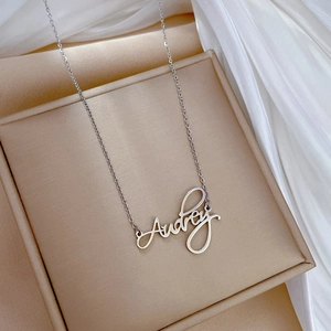 Macro shot of silver Audrey name necklace on beige jewelry box with silk background
