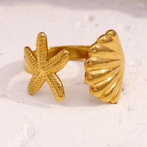 Close-up of gold plated starfish and shell ring on a white textured background