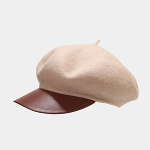 Detailed close-up of beige wool texture and brown leather brim on retro beret hat