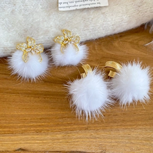 Close-up of golden flower stud earrings with crystals and white faux fur pom poms