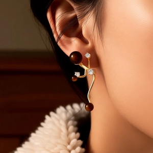 Macro shot of gold wavy earrings with brown tiger eye beads and pavé crystals on ear