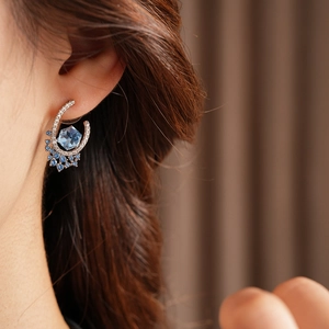 Close-up of a C-shaped silver ear cuff with blue hexagonal gems and sparkling zircon stones