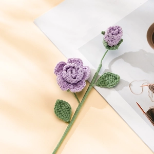 Detail view of handcrafted purple crochet rose with textured green leaves on beige background
