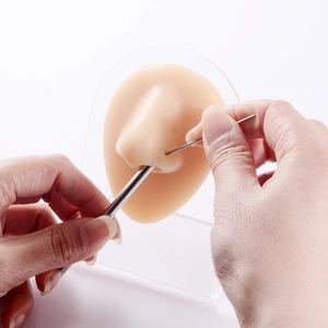 Macro shot of stainless steel piercing needle tool on silicone nose model for training