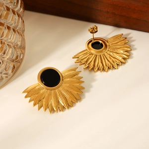 Detail of 18K gold fan leaf earrings with central black round stone inlay on white surface