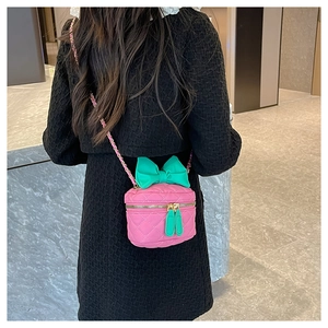 Detailed back view of a pink quilted cylinder bag with a large green bow and gold chain strap