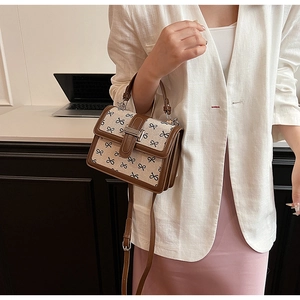Dettaglio borsa a tracolla in tela beige con finiture in pelle marrone e fiocchi neri