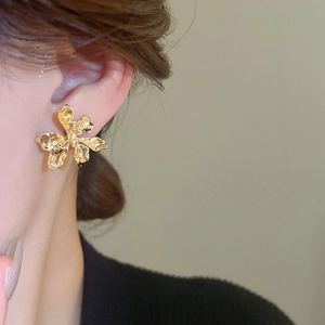 Close-up of golden metal flower stud earrings with detailed hammered texture on ear