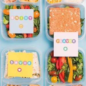 Flat lay of divided food containers with fresh salad and snacks on a blue background