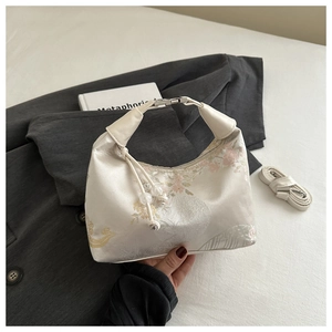 Close-up of beige satin jacquard handbag with floral embroidery and pearl handle details