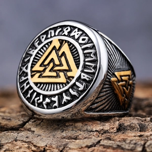 Macro shot of silver and gold Viking Valknut ring with runes on natural bark background
