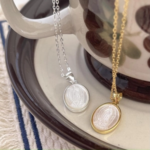 Virgin Mary shell necklaces in gold and silver tones hanging on a vintage coffee cup