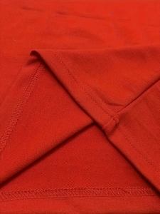 Detail view of red knitted fabric showing high-quality double stitching and hem finish