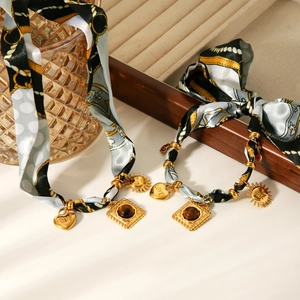 Detailed view of silk scarf necklaces with gold heart and sun pendants on a jewelry tray
