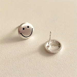 Macro detail of silver smiley face stud earrings showing brushed texture and polished back