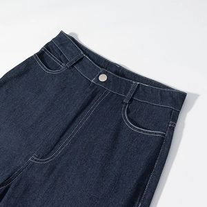 Détail de pantalon en denim bleu foncé avec surpiqûres blanches et bouton en métal