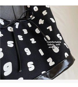 Detail of canvas tote with white numbers, leather bow tie and glossy leather base