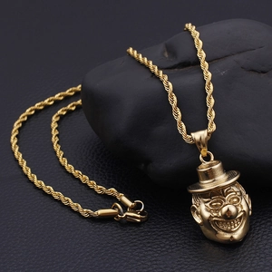 Detailed close-up of golden hip hop clown pendant on a twisted rope chain over dark rocks