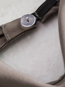 Detailed close-up of clear round button and durable tan twill fabric with black elastic band