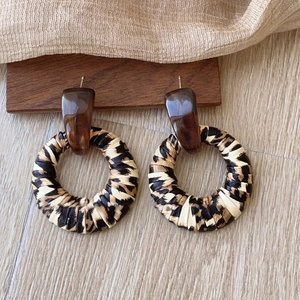 Leopard print woven hoop earrings with brown resin studs on a wooden background