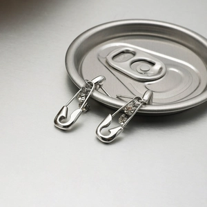 Detail of silver paperclip earrings with zircon inlays on a brushed metal background