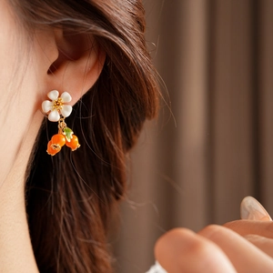 Detailed view of vintage flower and orange fruit pendant earrings on a female model