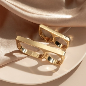 Close-up of two polished gold double-finger rings on beige plate with champagne silk