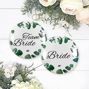 Detail of Team Bride tinplate badges with eucalyptus wreath design on white wood
