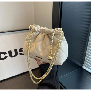 Detail of beige quilted chain bag with drawstring closure and gold ball accent