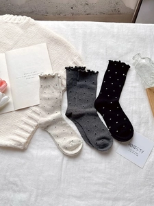 Detailed view of three pairs of polka dot socks with ruffled edges in cream, grey and black