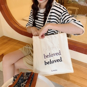 Détail de la broderie beloved sur le sac cabas en toile crème porté par un mannequin