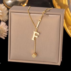 Detail of layered gold titanium necklace with letter F and square pendant on jewelry box
