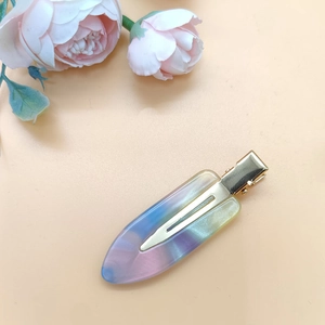 Close-up of rainbow gradient acetate hair clip with gold metal clamp on pink floral surface