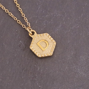 Detailed macro view of a gold hexagonal pendant featuring an embossed letter D on a chain